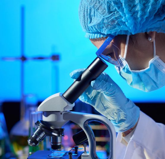 Profile view of concentrated Asian microbiologist examining sample with help of modern microscope while wrapped up in work at dim laboratory